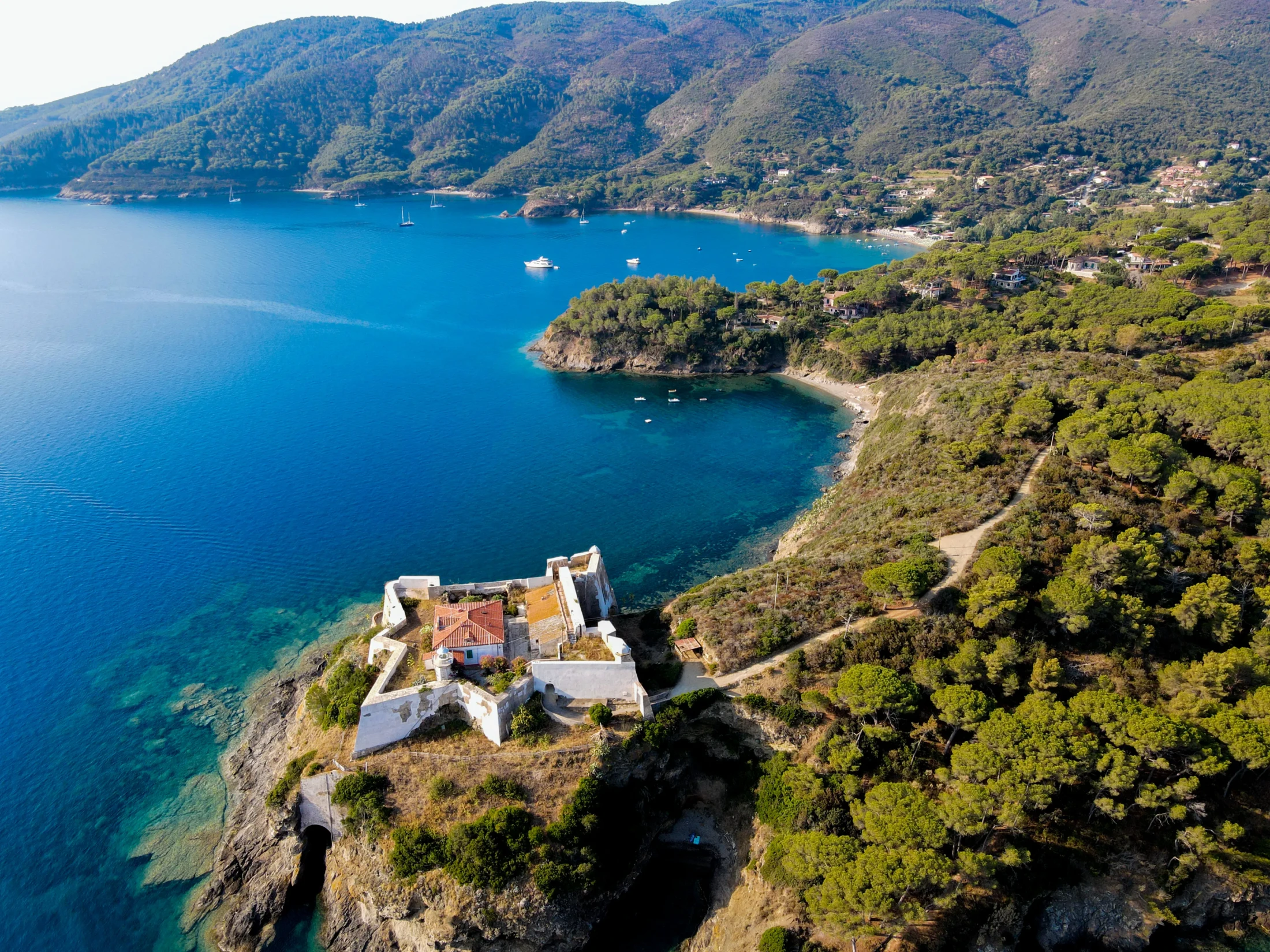 Vista aerea di una fortezza sulla costa dell'isola d'Elba con baia turchese e barche