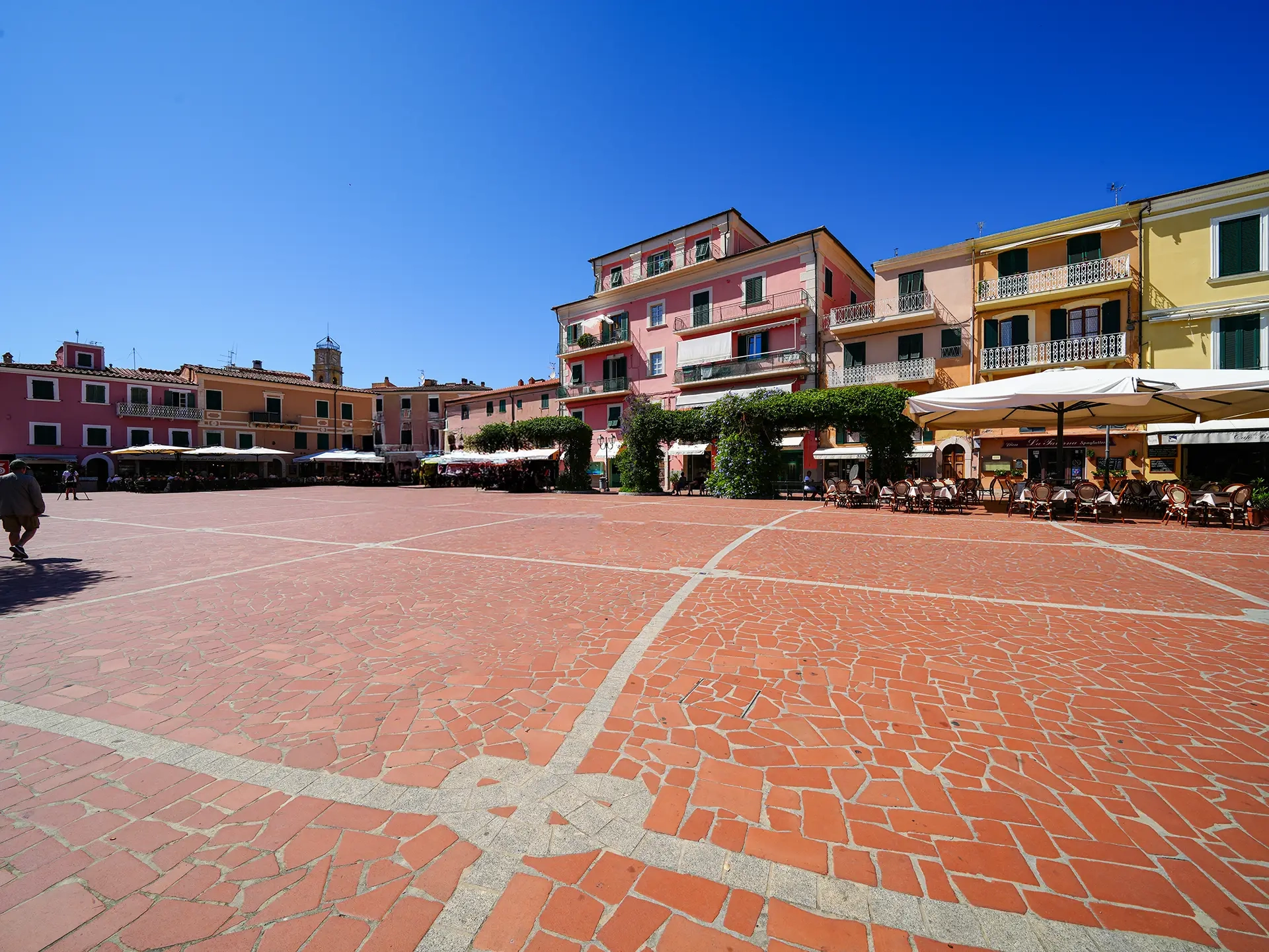 Piazza in pietra rossa circondata da case colorate e ristoranti all'aperto all'Isola d'Elba