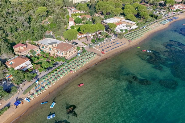 Vista aerea di un resort sulla spiaggia dell'Elba con ombrelloni, pineta e mare turchese cristallino