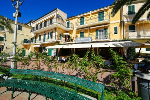 Panchina in ferro verde davanti a hotel giallo con balconi e terrazza ombreggiata all'Isola d'Elba