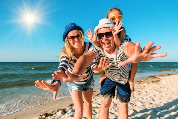 Famiglia sorridente in spiaggia all'Elba con braccia aperte verso il mare sotto il sole